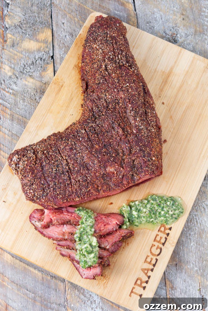 Traeger smoked tri-tip sliced on a cutting board topped with chimichurri