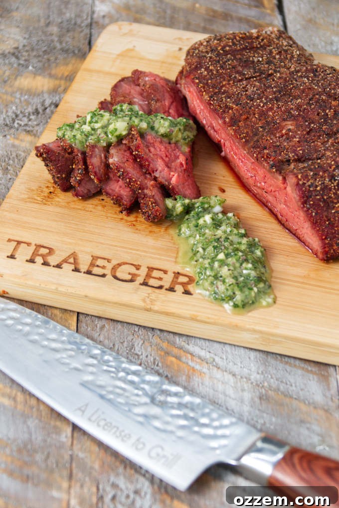 Traeger smoked tri-tip sliced on a cutting board topped with chimichurri