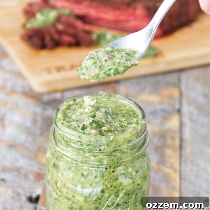 A mason jar filled with vibrant green cilantro chimichurri sauce, with sliced smoked tri-tip on the background on a cutting board, perfect for a summer BBQ.