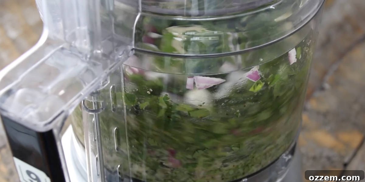 The chimichurri mixture being gently pulsed and blended in a food processor, showcasing its evolving vibrant green color and texture.