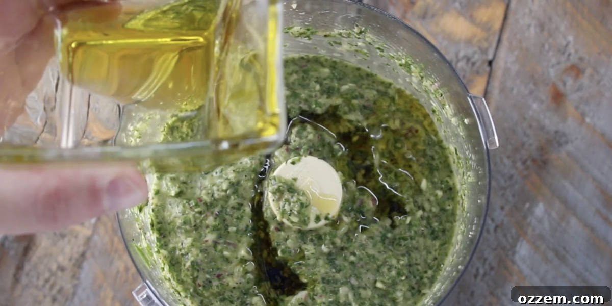 The remaining olive oil being poured into the food processor, completing the chimichurri mixture, ready for a final pulse to achieve the perfect consistency.