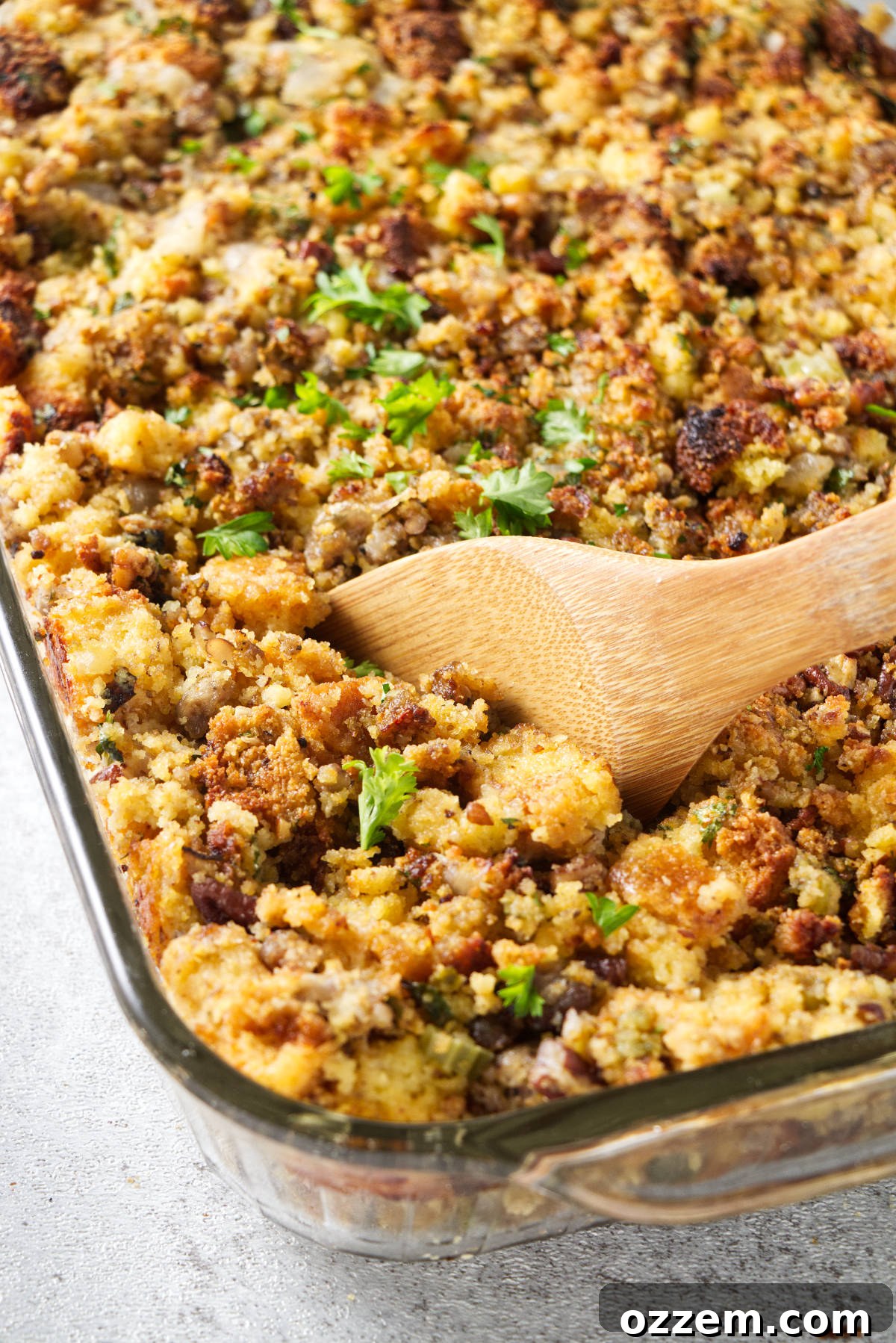 A wooden spoon serving a portion of delicious Traeger smoked cornbread stuffing from a casserole dish, ready for a holiday feast.
