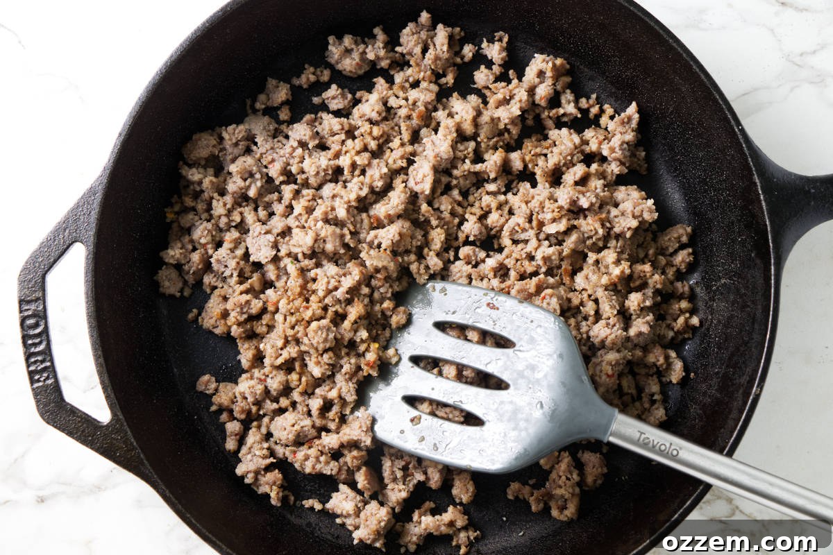 Ground sausage browning in a cast iron pan, preparing to be added to Traeger smoked cornbread stuffing.