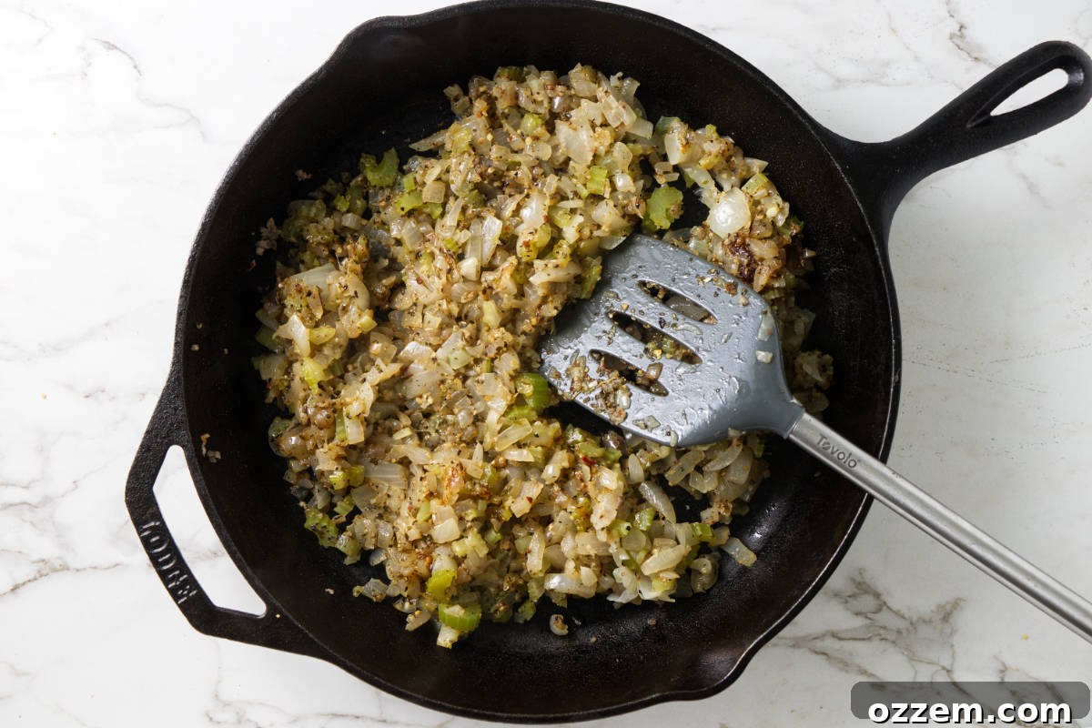 Onions and celery cooking in a cast iron pan, infusing with fragrant herbs and spices for the cornbread stuffing base.