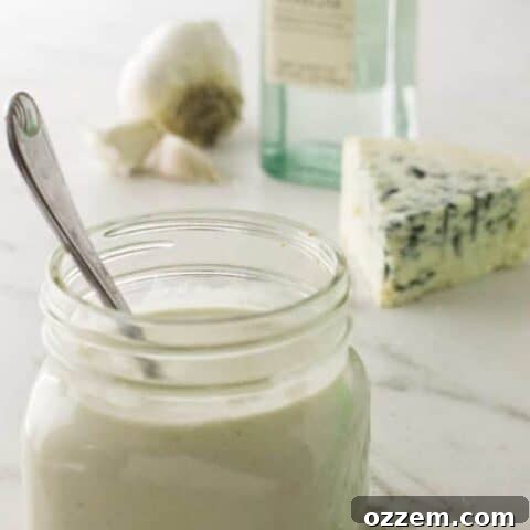 Mason jar filled with creamy homemade blue cheese dressing with a spoon, accompanied by a blue cheese wedge and fresh garlic.