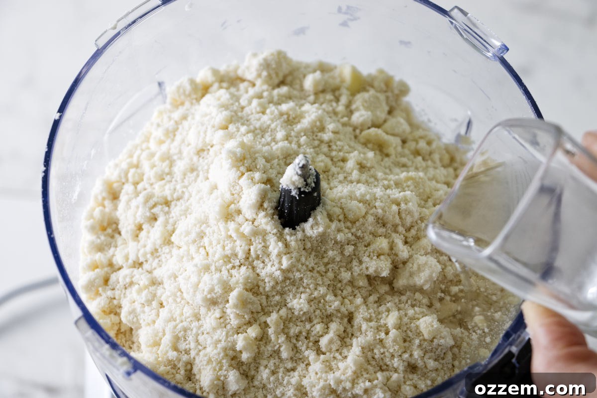 Adding chilled vodka and ice water to the pie crust ingredients in a food processor.