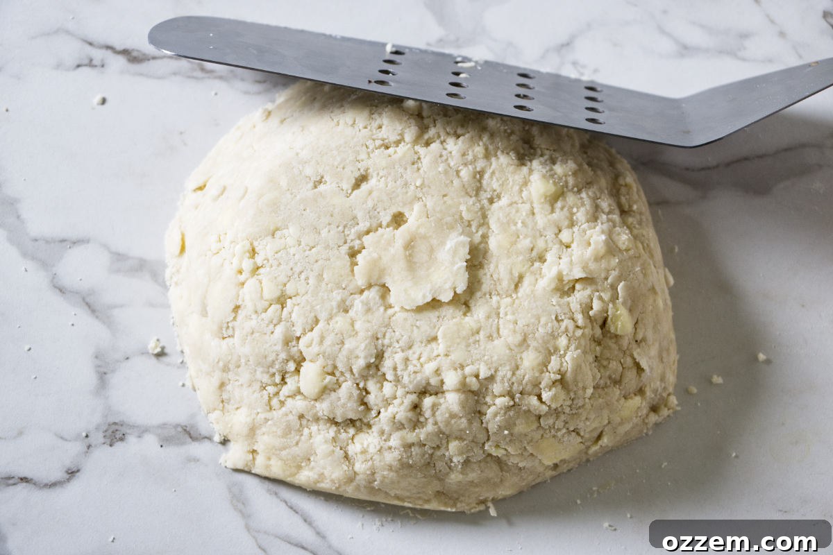 Gathering pie dough crumbs on the counter and pressing them together to form a cohesive ball.