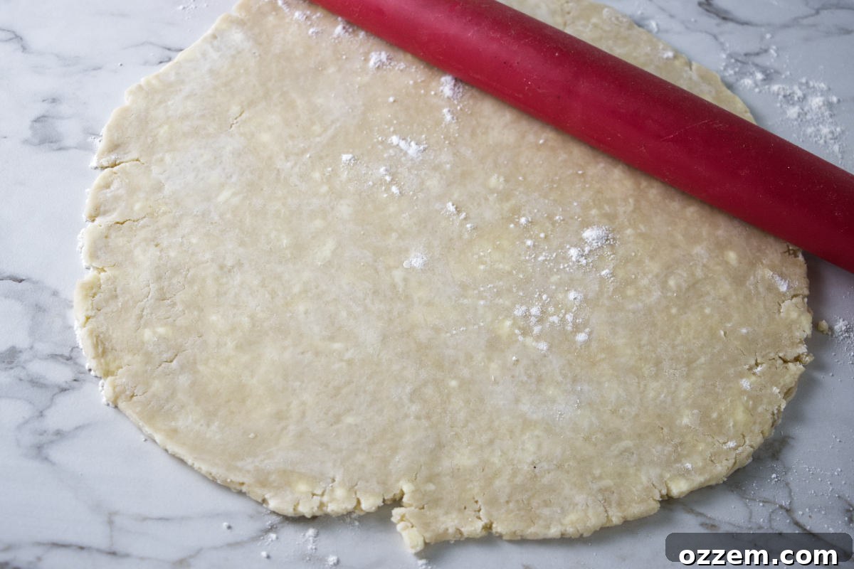 A baker expertly rolling out a chilled pie crust on a lightly floured surface.