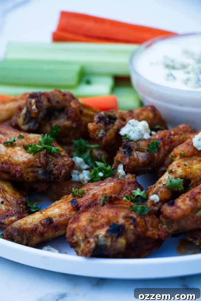 chicken wings with buffalo sauce sitting on a white plate with blue cheese and celery and carrots in the background