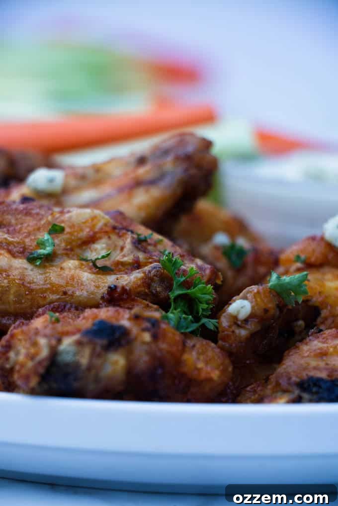 chicken wings with buffalo sauce sitting on a white plate with blue cheese and celery and carrots in the background