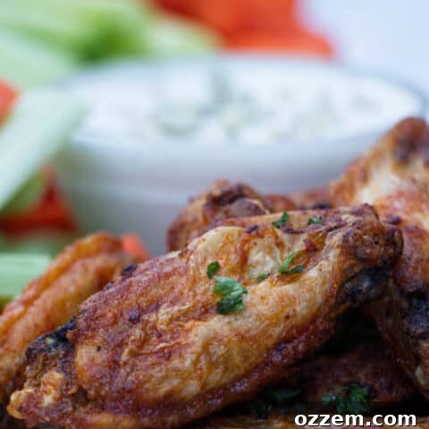 chicken wings with buffalo sauce sitting on a white plate with blue cheese and celery and carrots in the background