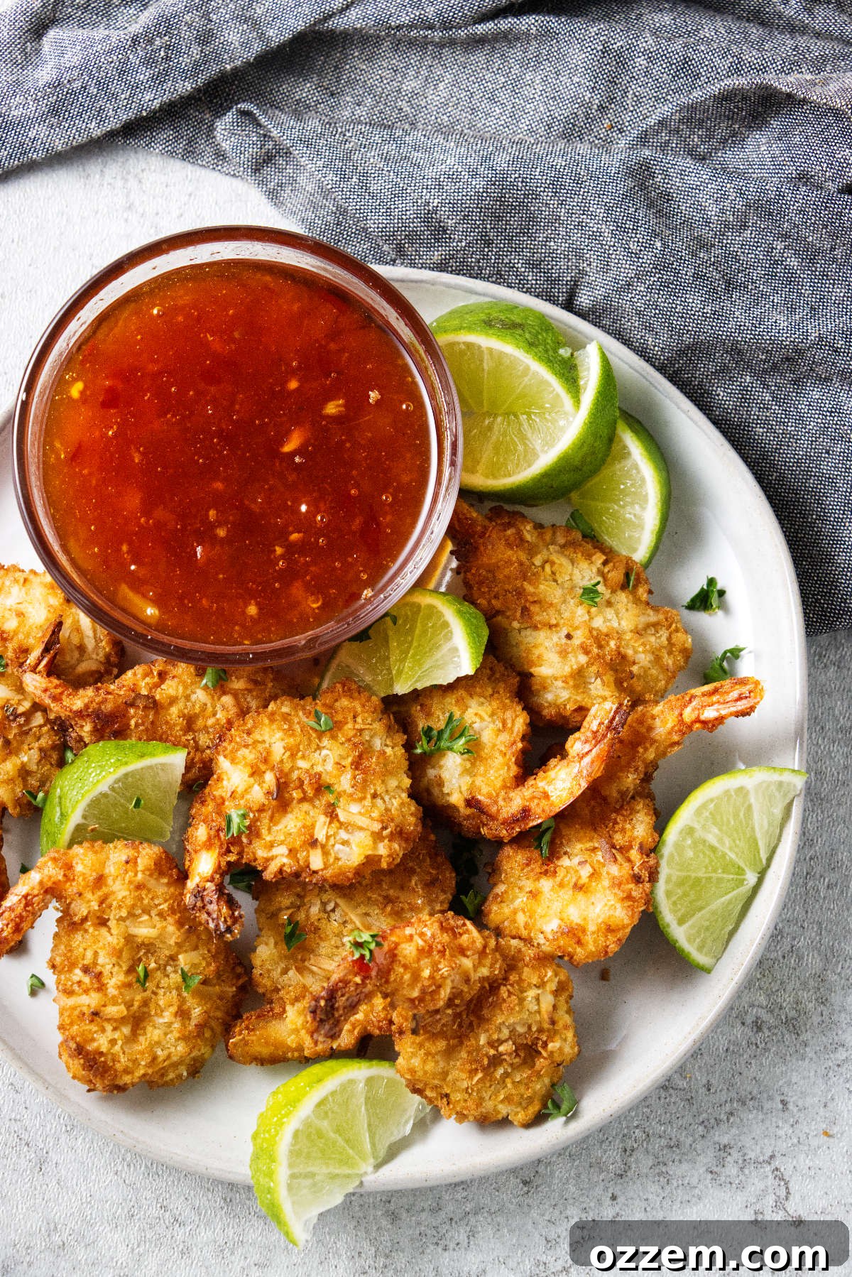 Crispy Air Fryer Frozen Coconut Shrimp 2 A plate of coconut shrimp and lime wedges next to a dish of dipping sauce.