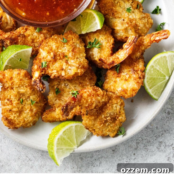 Coconut shrimp on a plate with lime wedges and chili dipping sauce.
