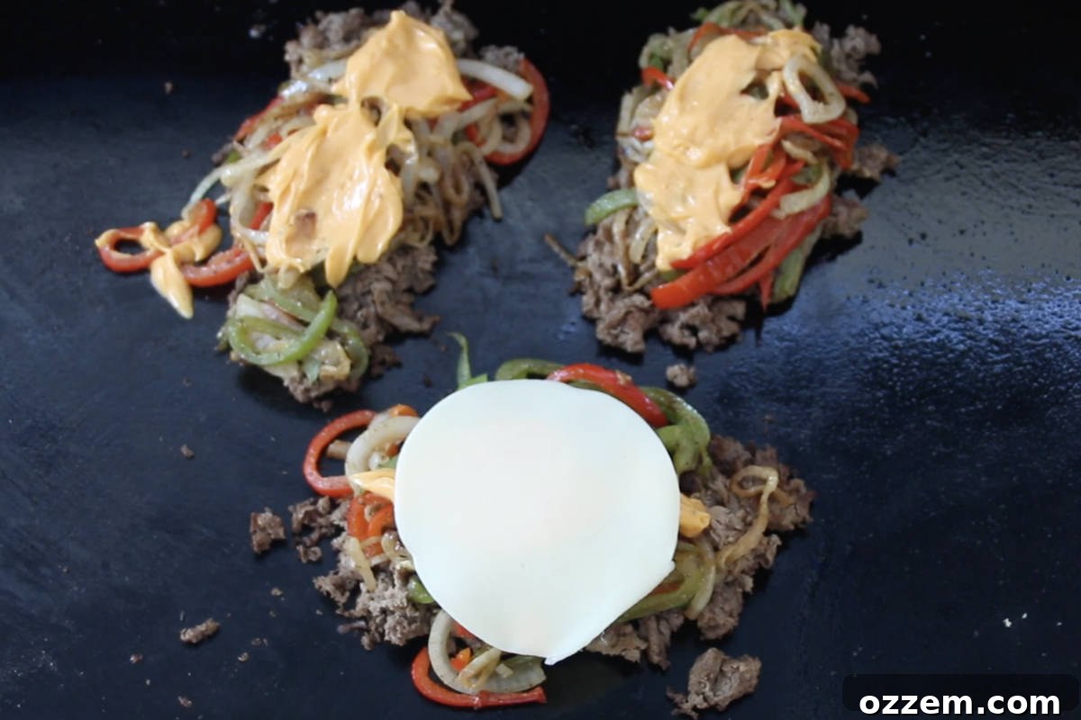 Sizzling Griddle Philly Cheesesteak 8 Three distinct piles of cooked sliced steak mixed with sautéed onions and peppers, generously topped with creamy Cheese Whiz and slices of provolone cheese, melting beautifully.