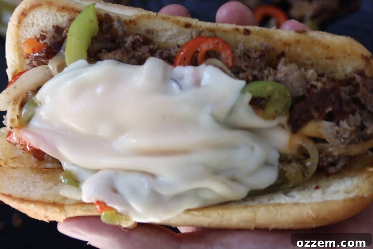 Sizzling Griddle Philly Cheesesteak 10 A finished Blackstone Philly cheesesteak sandwich being served onto a golden, toasted hoagie roll, ready to be enjoyed.