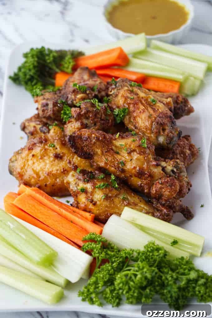 crispy air fried chicken wings sitting on a white plate with sliced carrots and celery with parsley sprinkled on top and dish of honey mustard in background