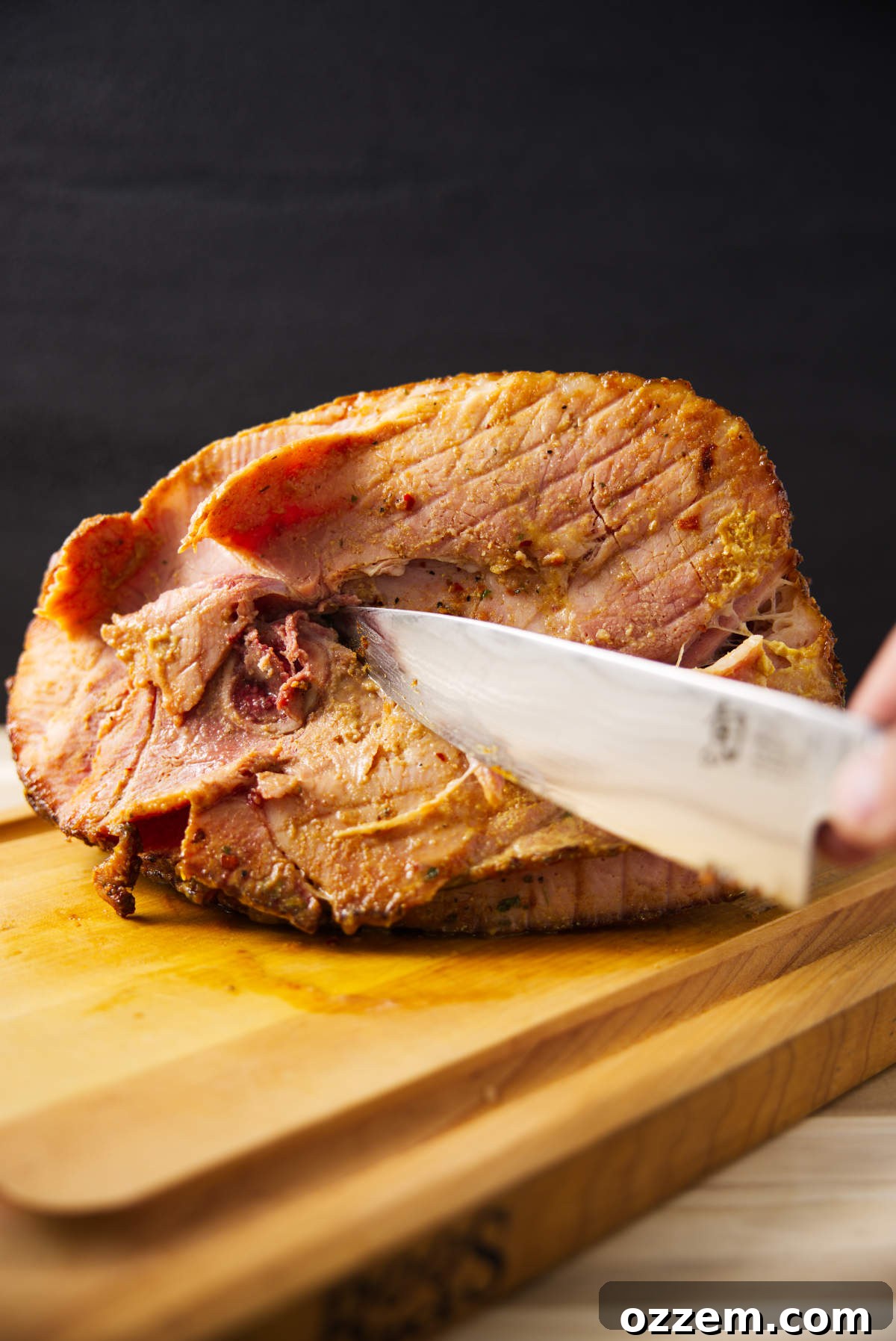 A close-up of a spiral sliced ham being expertly carved, with the bone removed, revealing juicy, glazed meat.