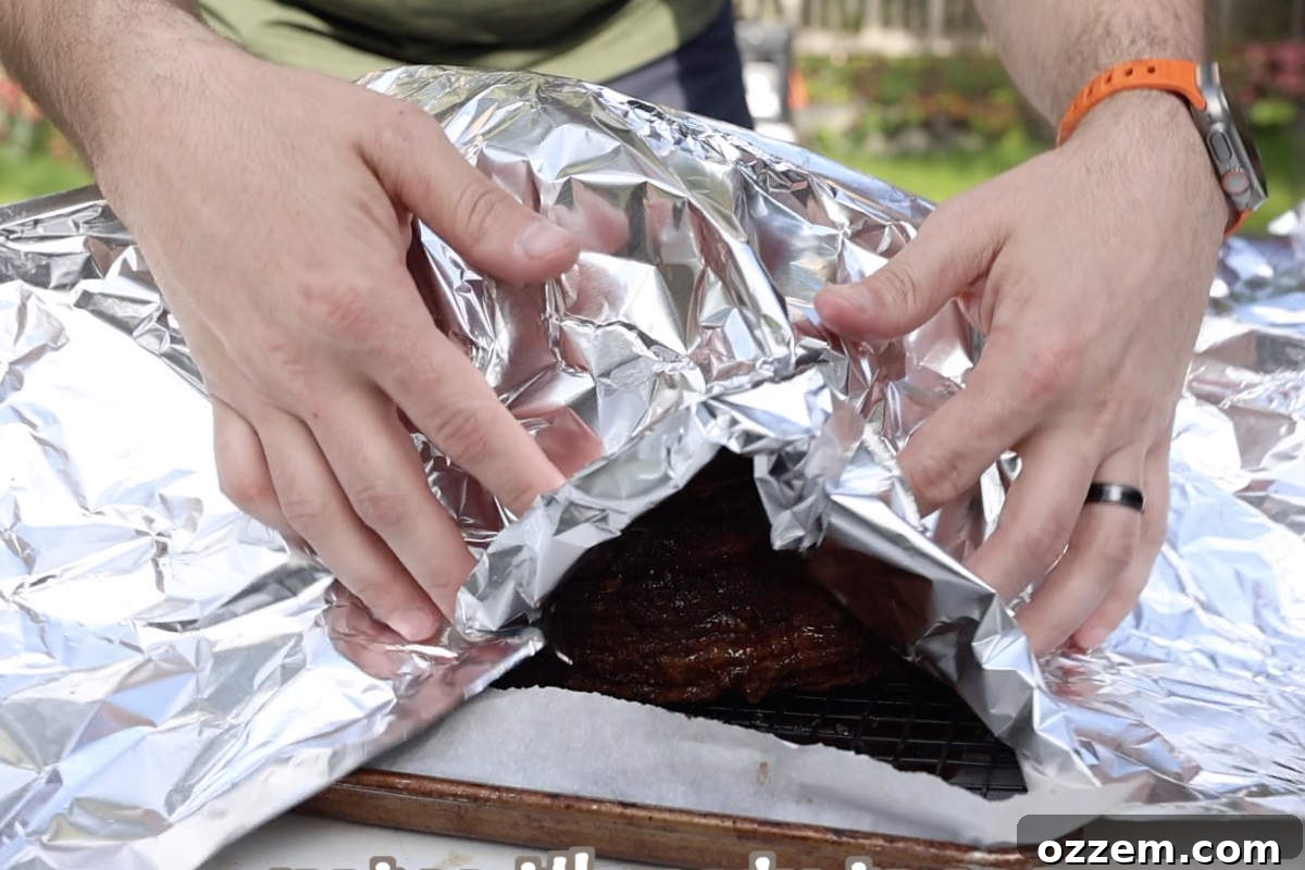 A double smoked ham, freshly removed from the smoker, tented loosely with foil and resting on a cutting board.