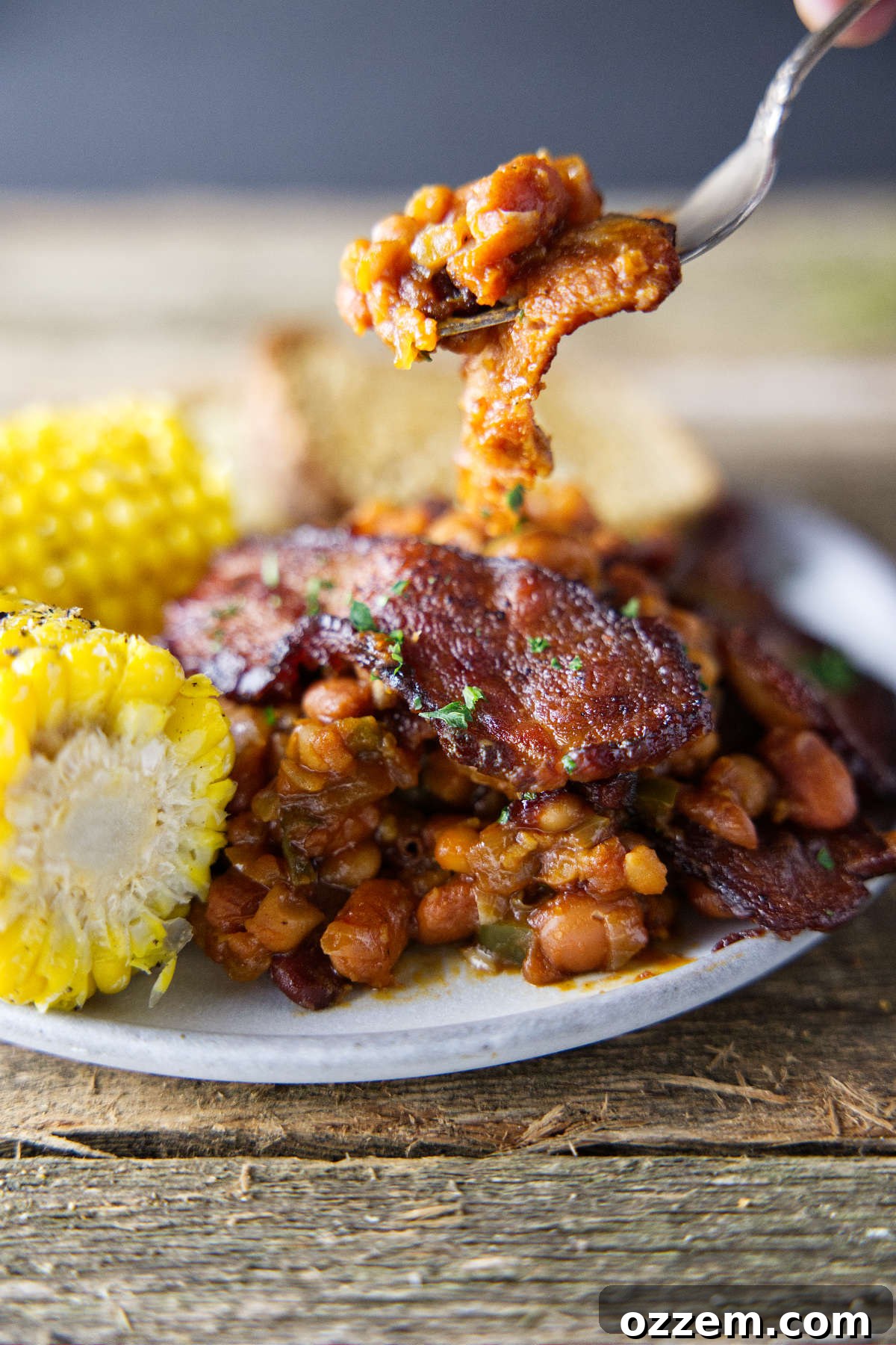 Pitmaster's Baked Beans 3 A fork full of delicious smoked baked beans, suspended over a plate, showcasing the rich, thick sauce and visible bean texture.