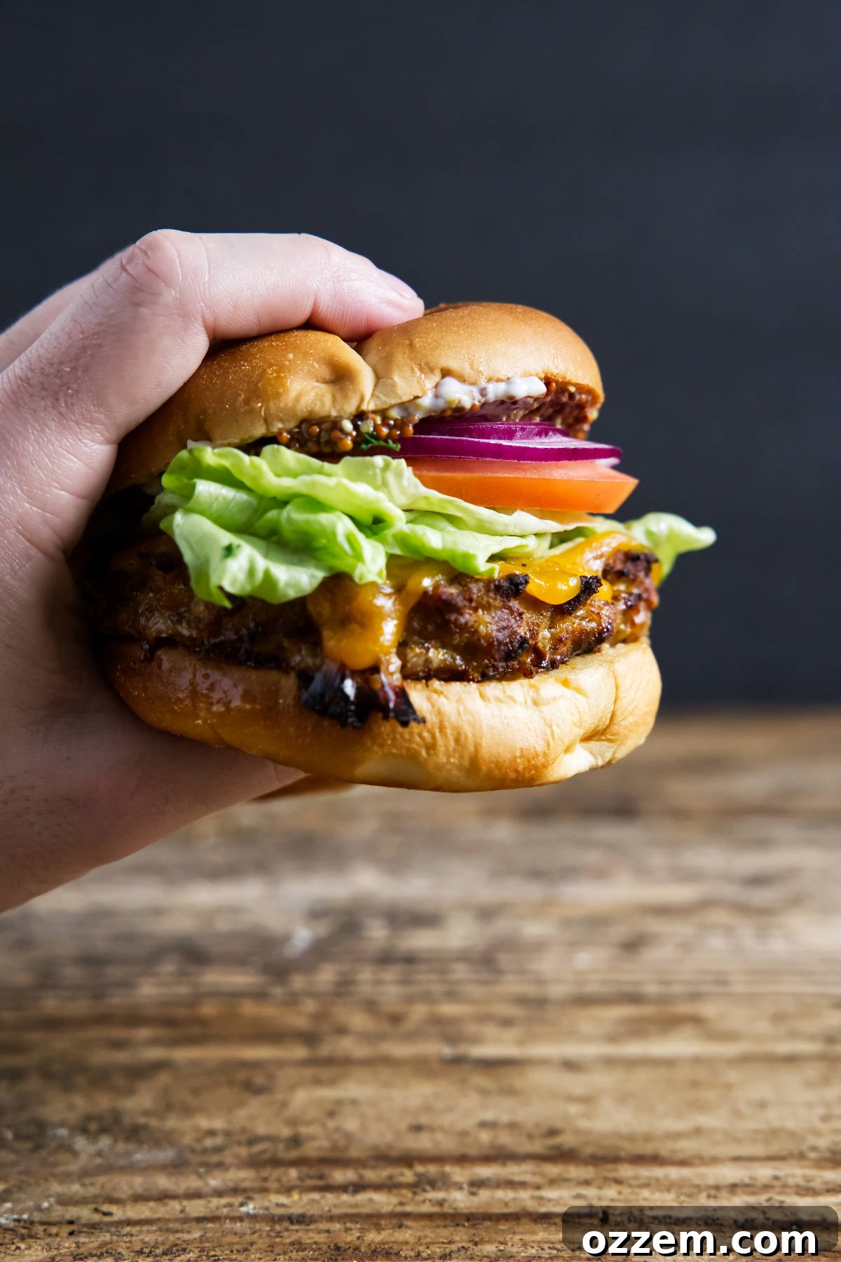 Fully assembled air fryer turkey burger being held by hand with melted cheese oozing out, nestled in a brioche bun with fresh toppings.
