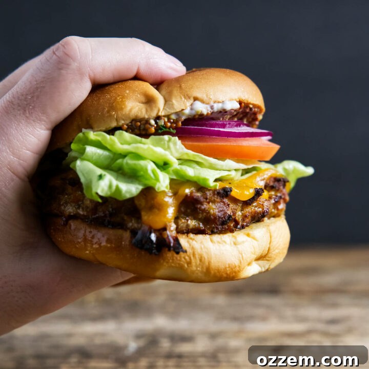 Fully assembled turkey burger being held by hand with cheese oozing.
