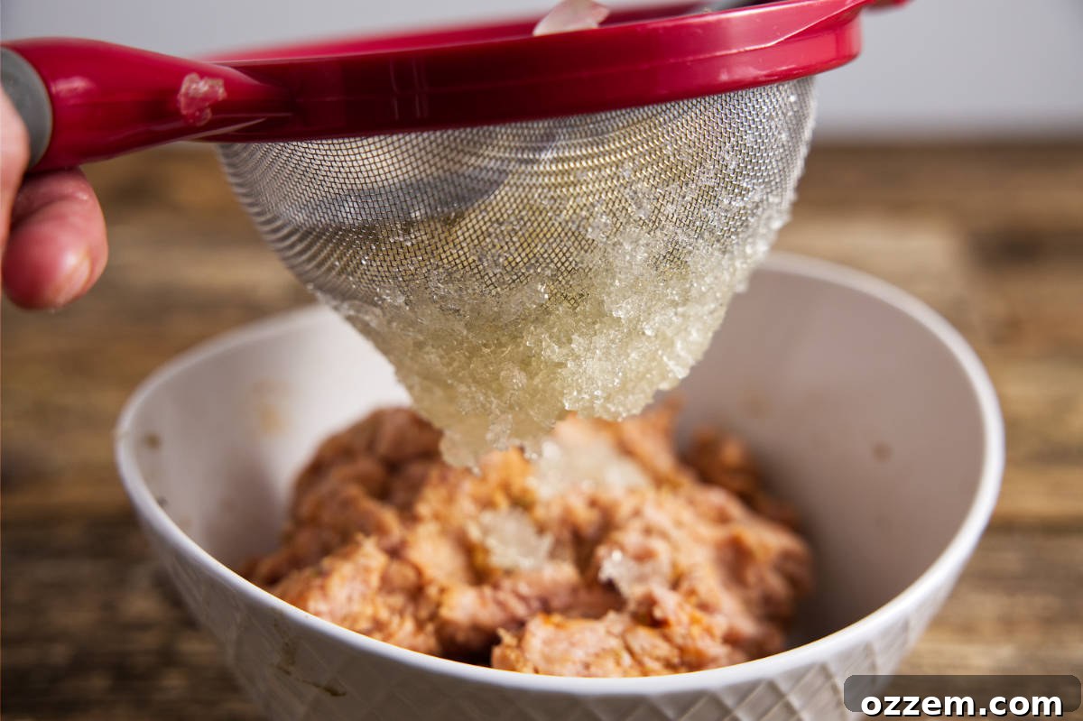 Pushing the set chicken stock gelatin through a mesh strainer with a spoon to create small granules.