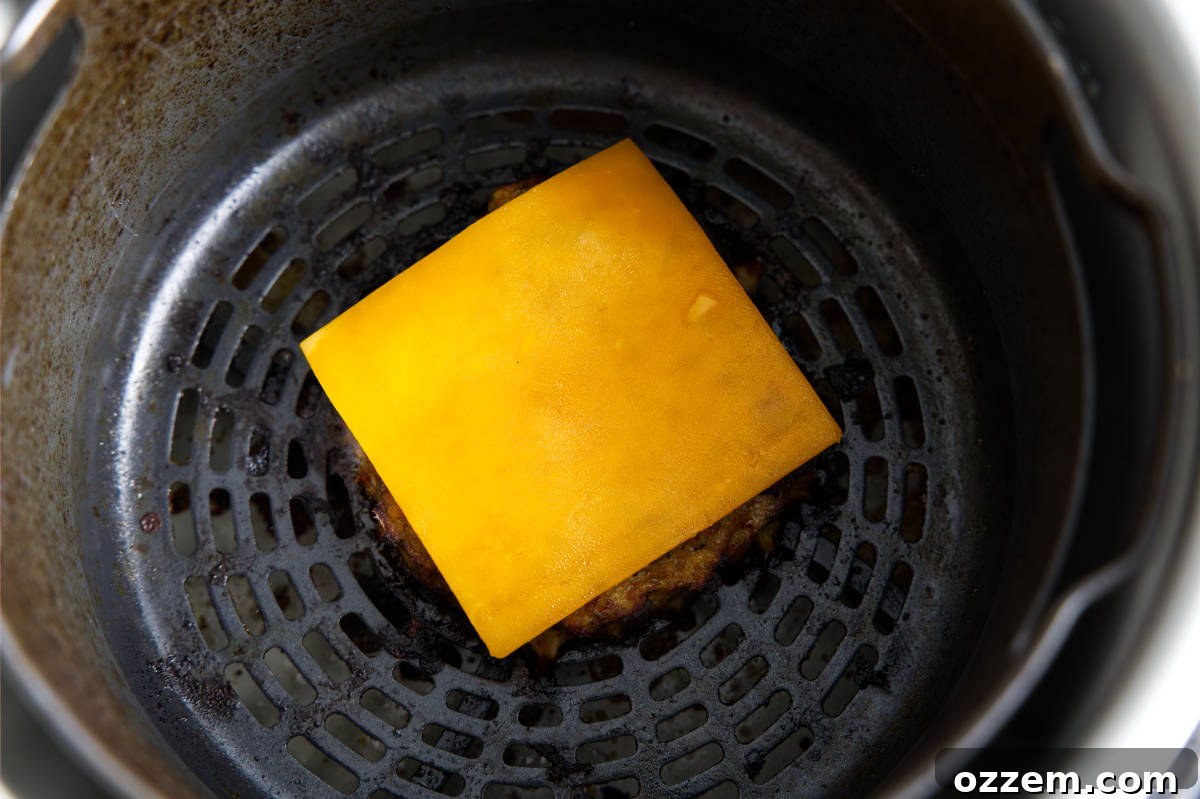 A slice of cheddar cheese melting on top of a cooked turkey burger patty inside the air fryer.