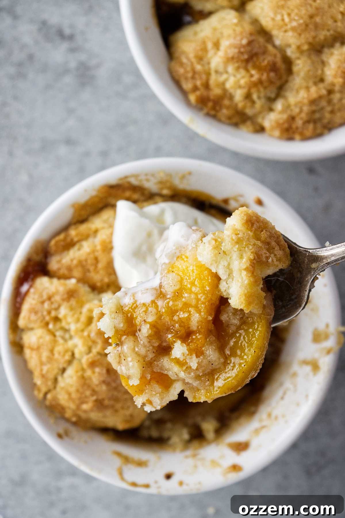 a fork full of peach cobbler hoving over a ramekin filled with the dessert