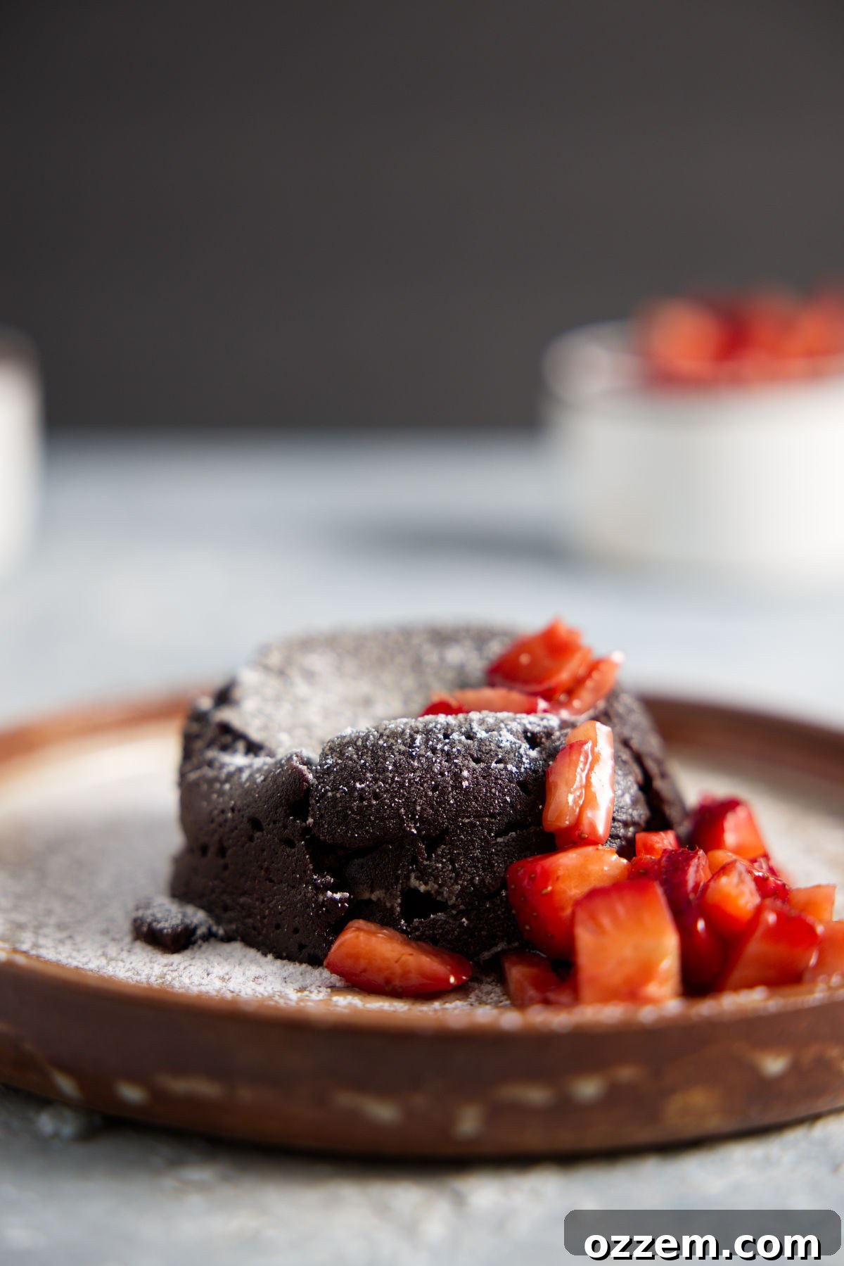 Air fryer mug cake plated with chopped strawberries and dusted with powdered sugar.