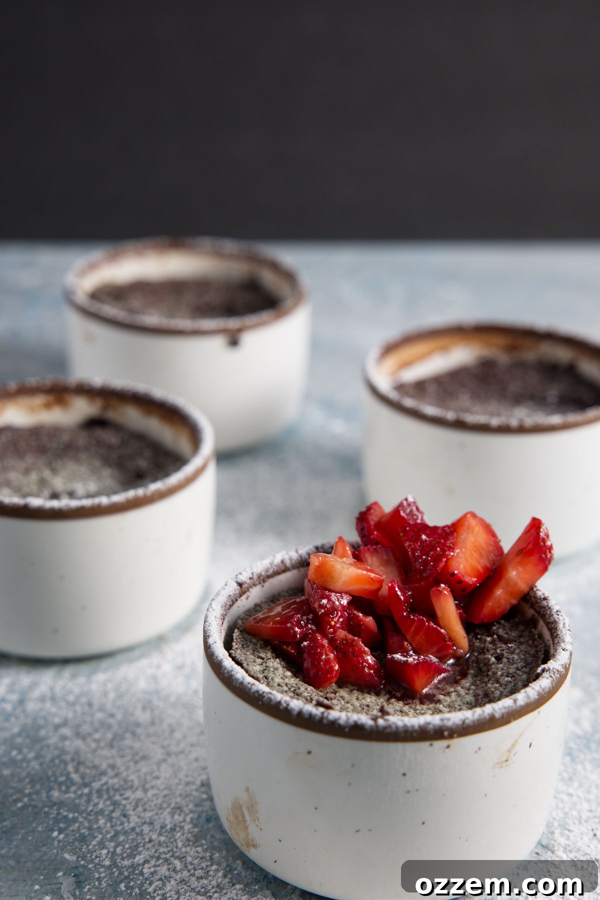 Several air fryer lava cakes in ramekins and topped with chopped strawberries.