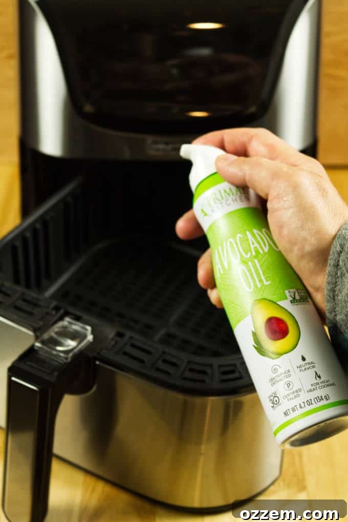 Air Fryer Mastery: Essential Tips and Tricks 3 A bottle of avocado oil aerosol spray positioned in front of a sleek stainless steel and black air fryer on a warm wooden table, highlighting a preferred oil choice for air frying.