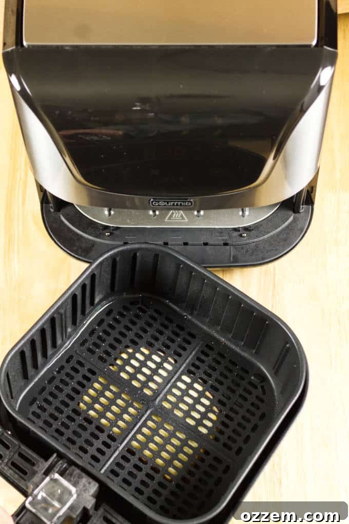 Air Fryer Mastery: Essential Tips and Tricks 5 A black and stainless steel air fryer with a slice of bread positioned underneath its removable basket and pan, resting on a wooden table, illustrating a method to soak up grease.