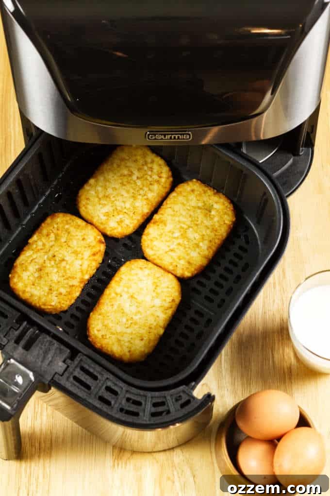 Air Fryer Mastery: Essential Tips and Tricks 7 Crispy hash browns perfectly spaced in a black and stainless steel air fryer basket, with a breakfast setting including eggs and milk on a wooden table.