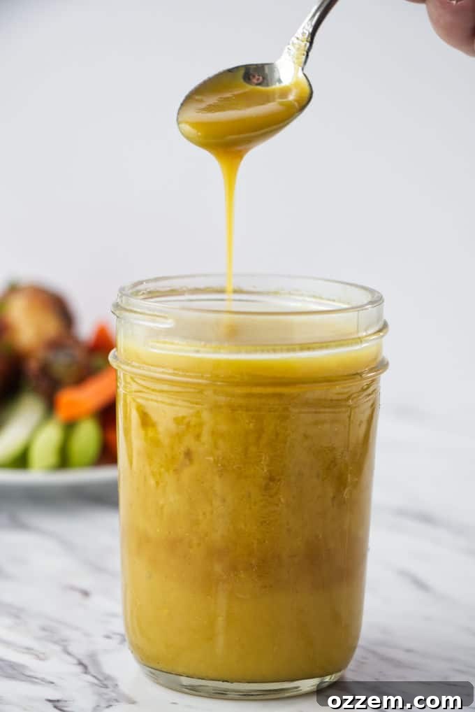 Liquid Gold Mustard 2 Brownish yellow honey mustard sauce in a mason jar with chicken wings, carrots, and celery on a white plate in the background