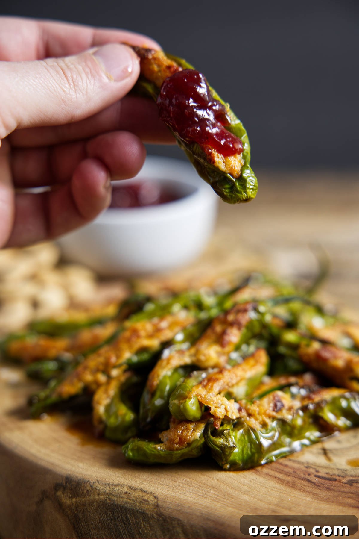 Air fryer stuffed shishito peppers, one held in fingertips with a red cherry preserves topping