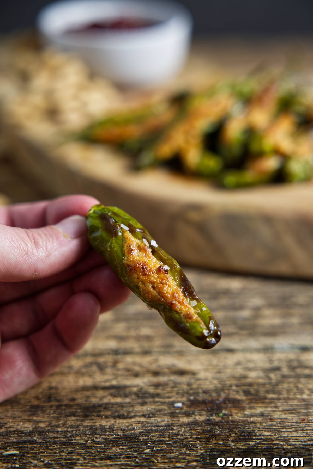 Single stuffed shishito pepper with charred and blistered skin, stuffed with cheese, on a dark background