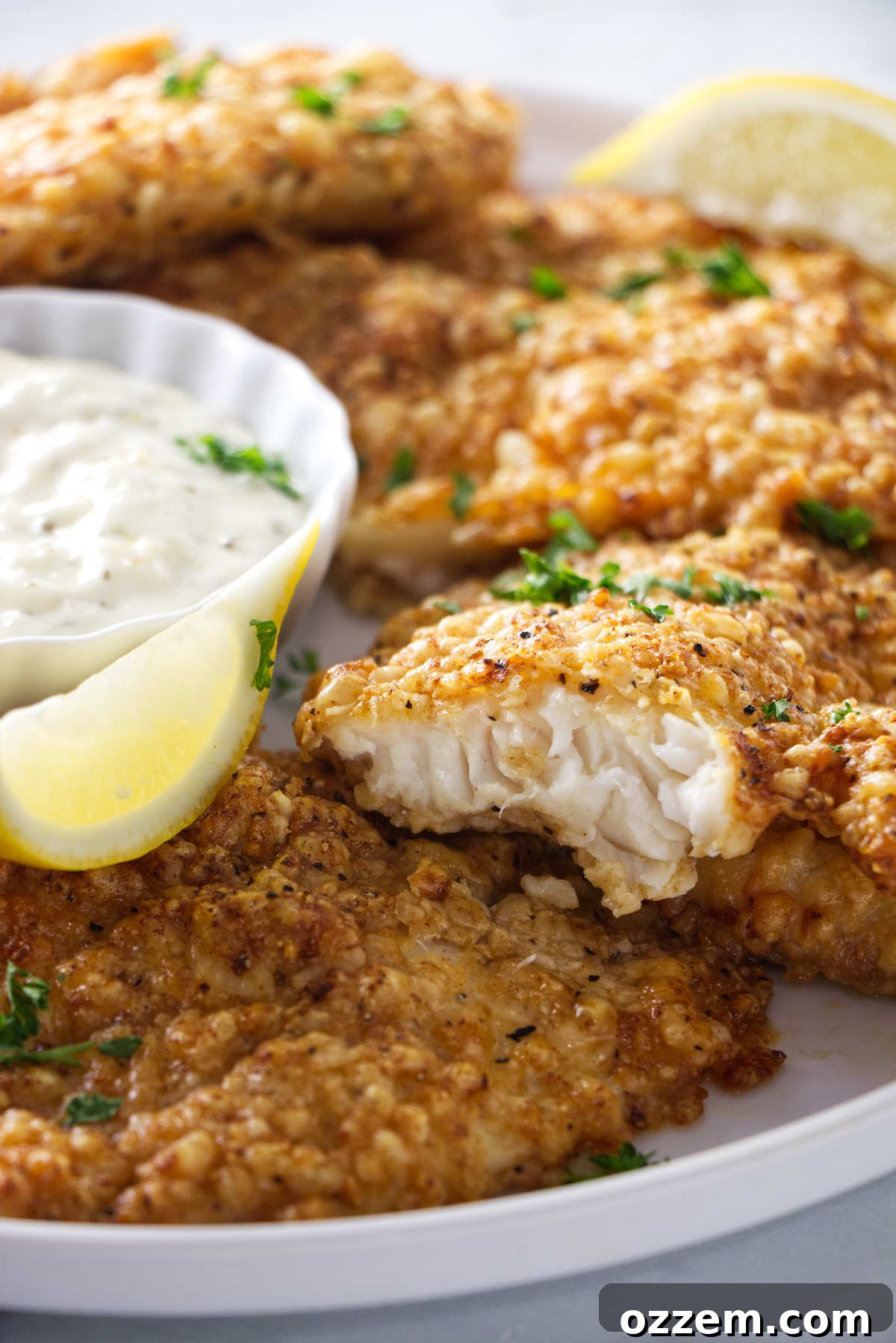 Crispy air fryer tilapia fillets seasoned with Parmesan, served golden brown on a white plate with lemon wedges and fresh parsley.