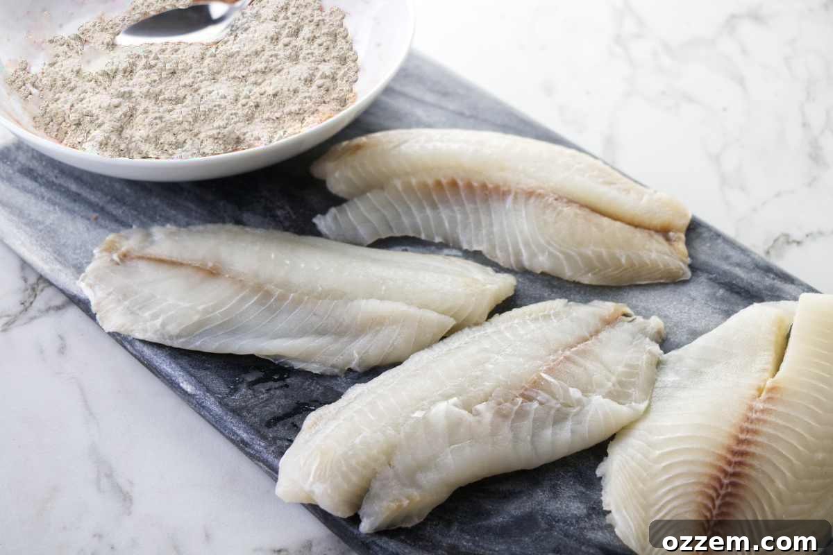 Fresh, raw tilapia fish fillets alongside a bowl of all-purpose flour on a wooden cutting board, ready for breading.
