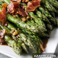 Cooked asparagus on white plate with chopped bacon and onion vinaigrette.