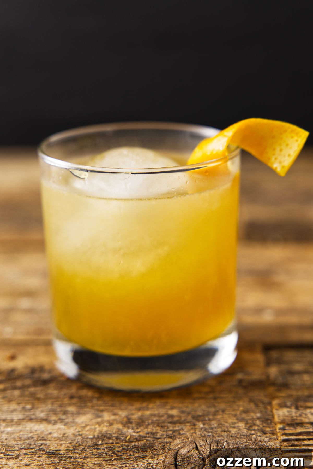 Glass filled with orange bourbon cocktail with orange peel twist and globe ice.