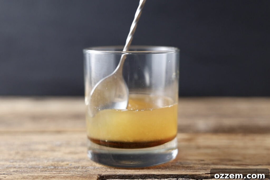 Stirring maple bourbon smash in glass.
