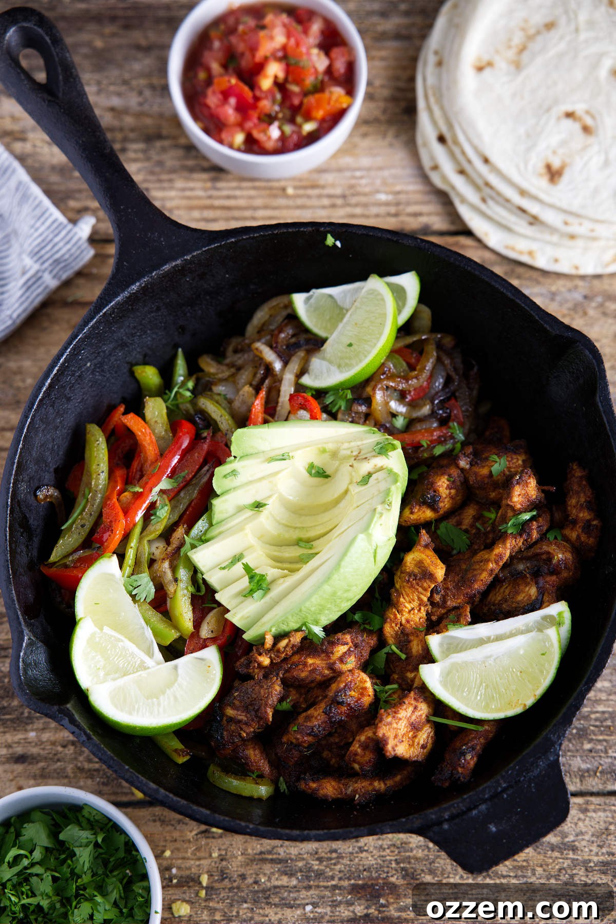 A rustic cast iron pan brimming with perfectly caramelized chicken fajitas, garnished with fresh lime wedges and creamy avocado, surrounded by warm tortillas, vibrant salsa, and fresh cilantro, creating an inviting feast.
