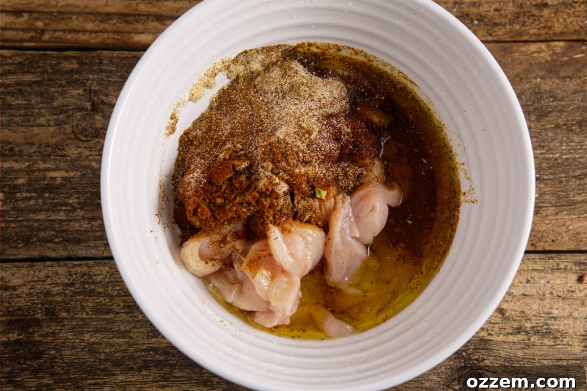 A large mixing bowl filled with thinly sliced chicken breast, with a hand pouring in the vibrant marinade ingredients.