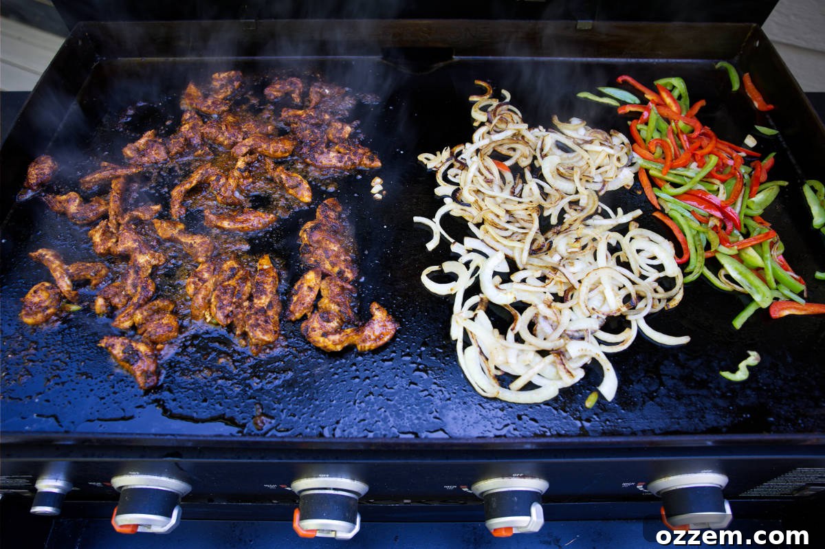Vibrant chicken fajitas cooking on a hot Blackstone griddle, with chicken, colorful bell peppers, and onions neatly separated before combining.
