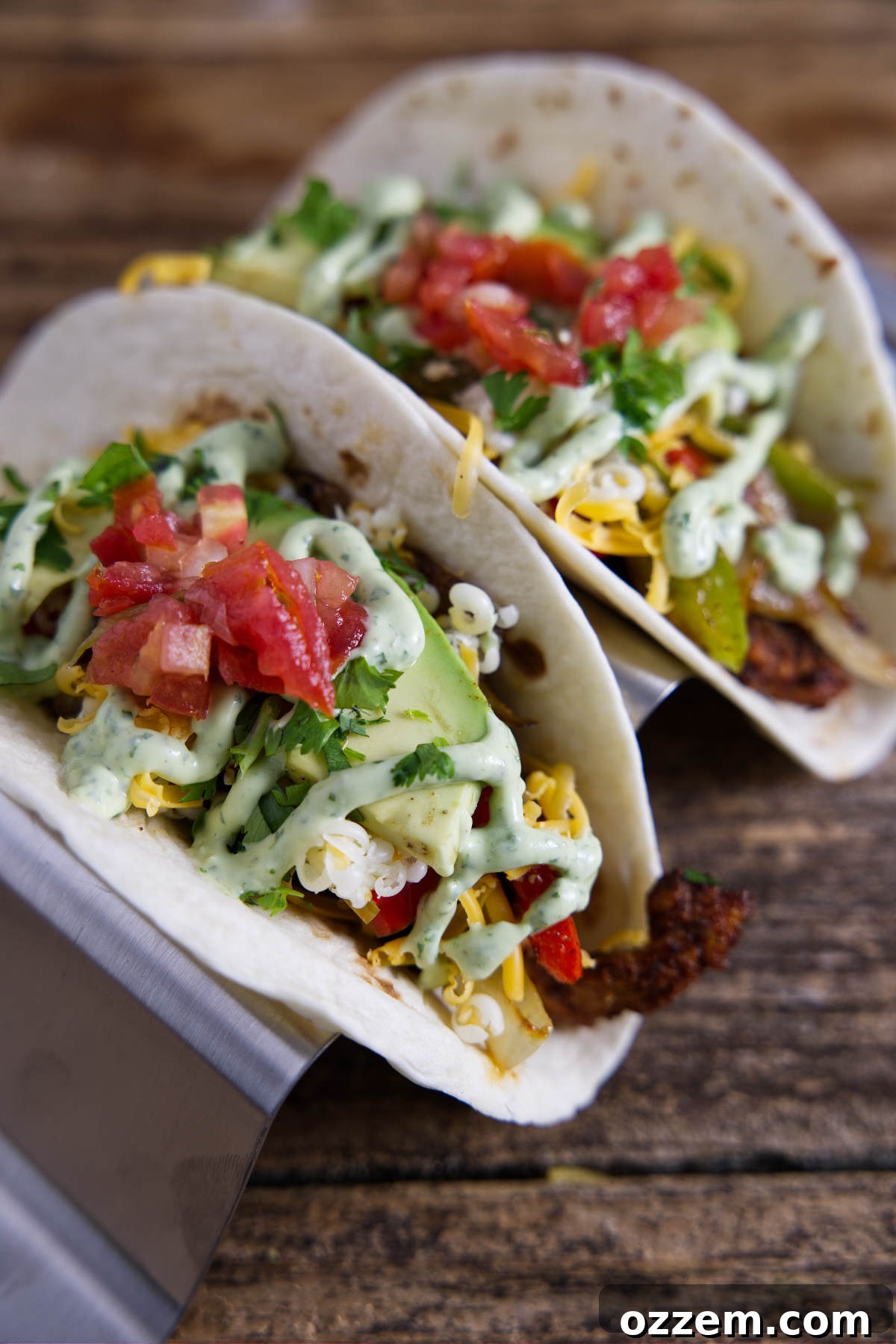 A close-up view of delicious Blackstone Fajitas served in warm tortillas, beautifully garnished with a drizzle of creamy avocado crema and fresh, vibrant bell peppers.