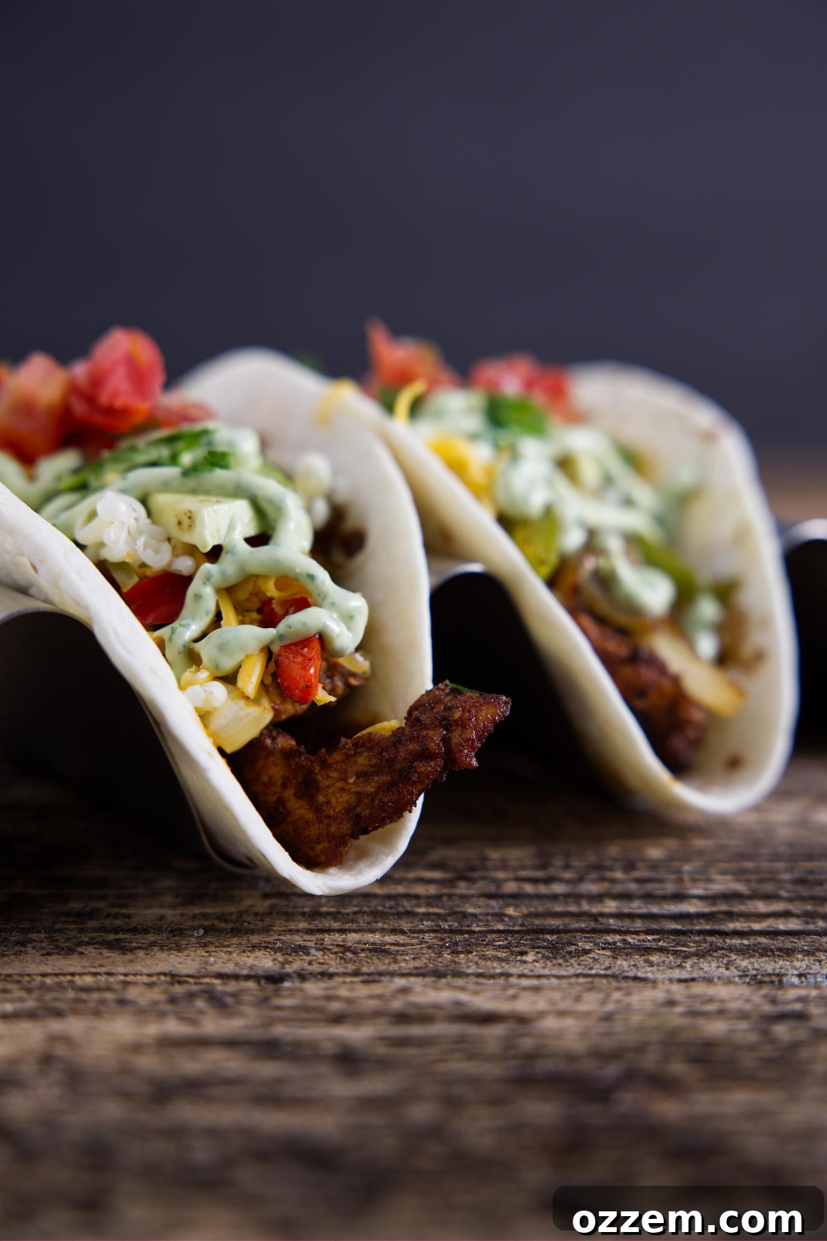 Two perfectly assembled tacos, generously filled with savory Blackstone fajita mixture and elegantly drizzled with a rich avocado crema.