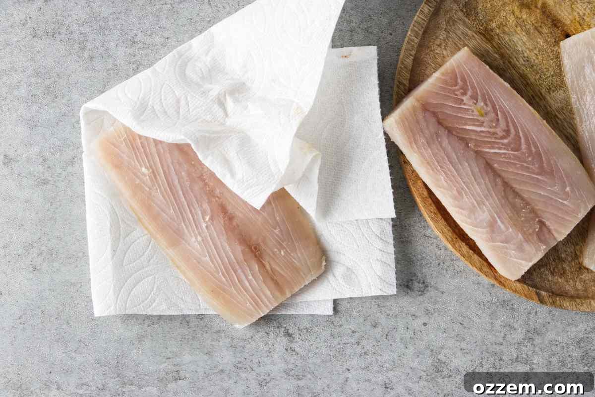 Golden Air Fryer Mahi Mahi 5 A hand gently patting a mahi mahi fillet dry with a paper towel, a crucial step for optimal seasoning.