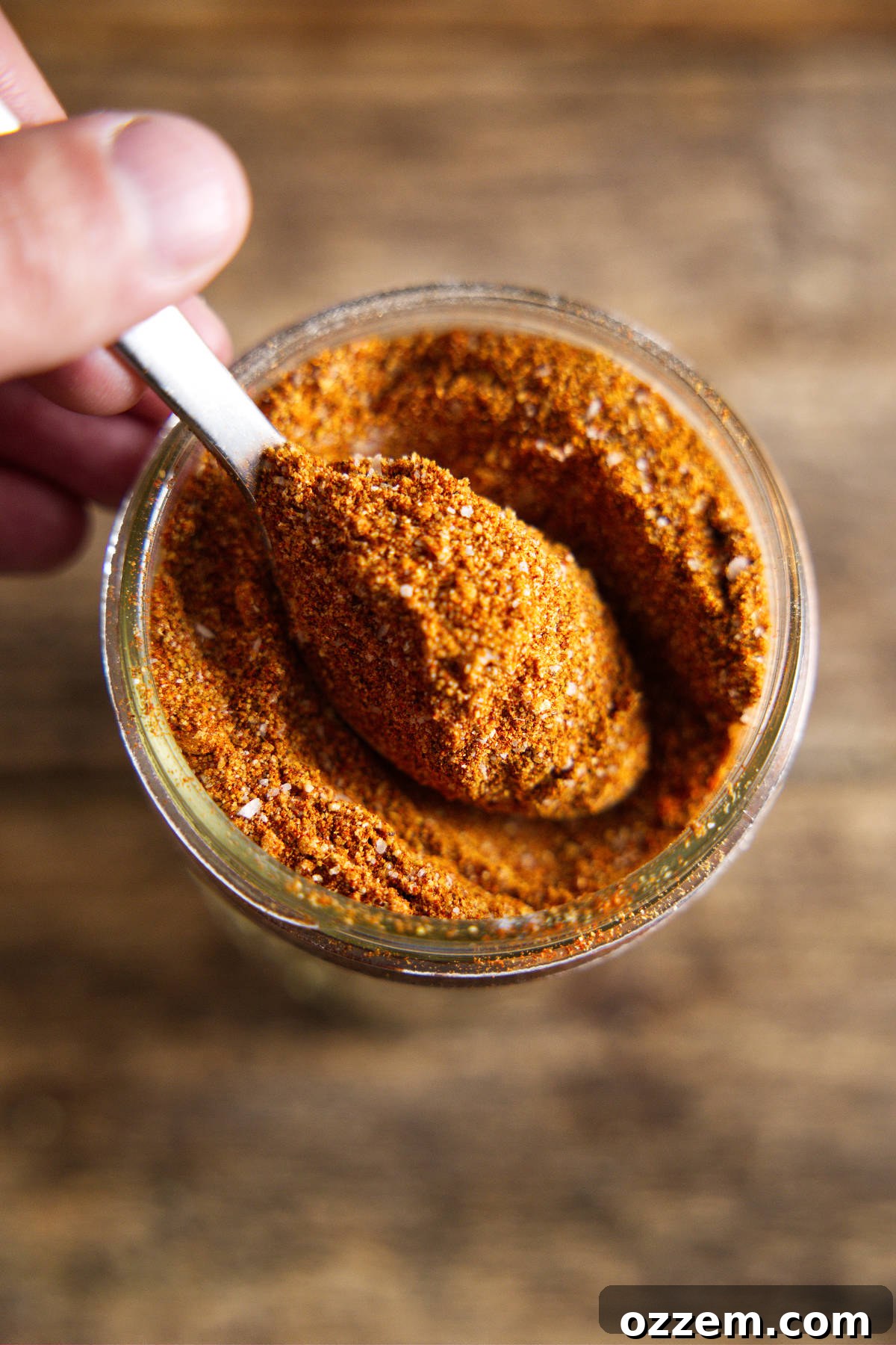 A wooden spoon overflowing with the rich, reddish-brown homemade pork butt rub, showcasing its finely blended texture.