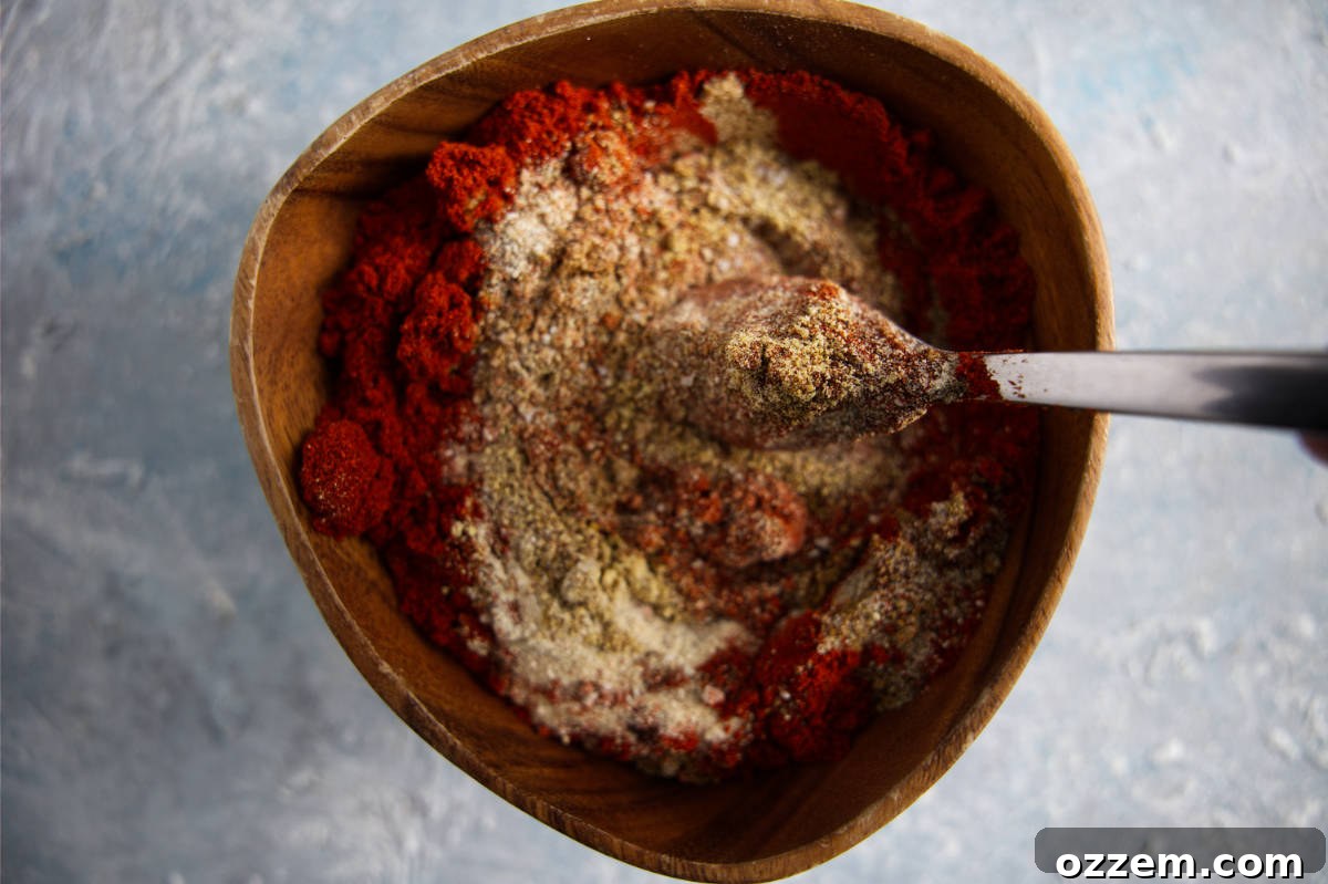 A close-up shot of hands mixing the various dry rub ingredients together in a large stainless steel bowl with a whisk.