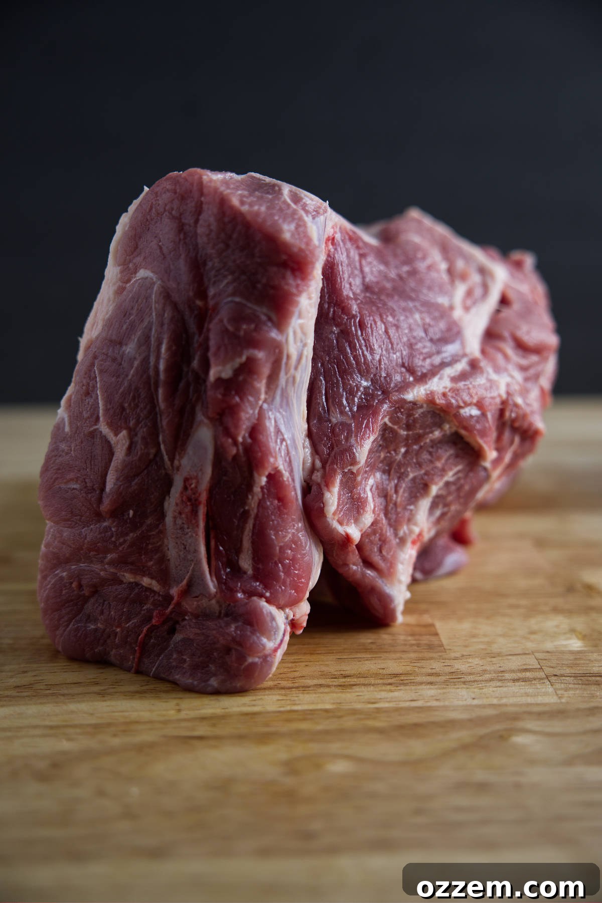 Close-up of a raw pork butt cut, showing generous intramuscular fat and marbling, ideal for slow cooking.
